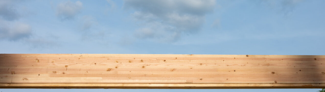 Overhead wood glue laminate, glulam, header beam with blue sky and puffy white clouds in background, housing development project under construction
