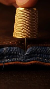 Close up of thimble pushing needle through leather and denim fabric.