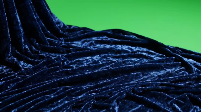 Elegant dark blue velvet fabric flowing and rippling with light reflections on a green screen background for easy chroma key editing and creative compositing.