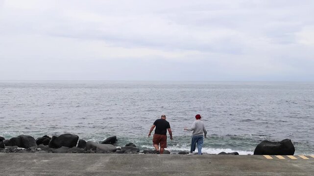 People standing and observing the sea, in beach or seaside promenade, with people, seawall, rocks, with concrete, rock texture, from a wide-angle shot from a low perspective perspective.