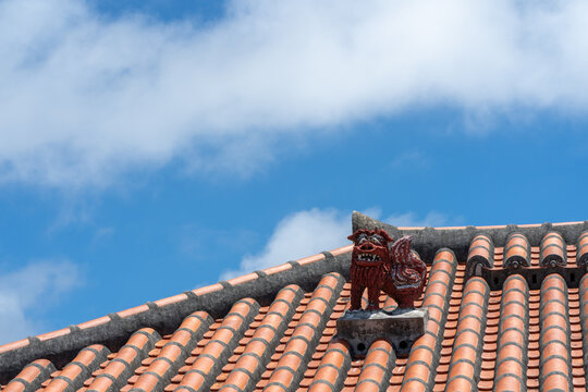 Red shisa guardian statue on tiled roof against blue sky