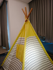 A children's play teepee tent made of fabric with a grey zigzag pattern and bright yellow accents, standing indoors © awgraphoto