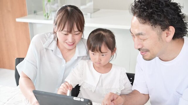 自宅のダイニングやリビングでペンでタブレットを使って家庭学習をする親子3人の家族とデジタル教育のイメージの動画
