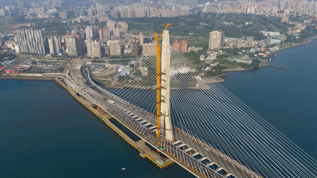 Aerial view of the Danjiang Bridge under construction with its tall pylon and cable-stayed design spanning the Tamsui River, near the skyline of Tamsui District, New Taipei City, Taiwan.