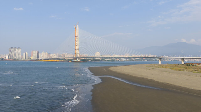 Aerial view of the Danjiang Bridge under construction spanning the Tamsui River with a sandy beach and city skyline in the background in Tamsui District, New Taipei City, Taiwan.