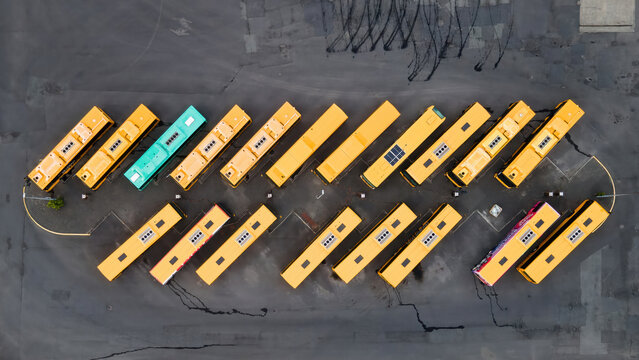 Aerial view of a bus depot with rows of yellow buses parked in an orderly pattern on asphalt in Reykjavik, Reykjavikurborg, Iceland.