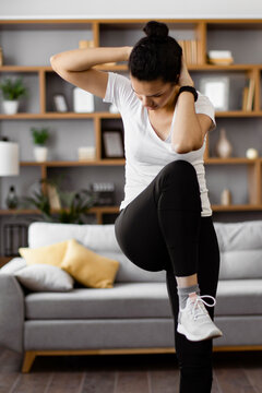 A young woman performs an abdominal crunch exercise while standing in her living room, focusing on her fitness routine