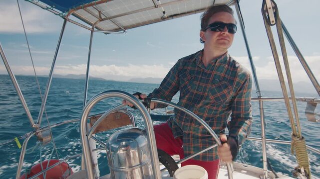 Young man sailor sailing alone the small sailing boat in the fresh sea during nice sunny day. Sailor enjoys the wind. Confident sailor steers the sail boat