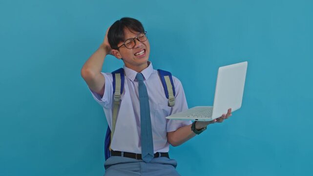 Male student in uniform feeling confused or defeated while studying on laptop computer