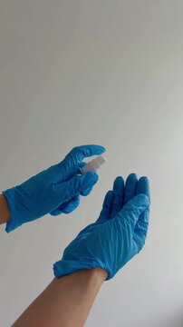 Person wearing blue protective gloves using hand sanitizer spray isolated on a white background, demonstrating proper disinfection procedures for hygiene and safety
