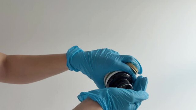 Nurse wearing blue nitrile gloves pouring vitamin pills into a hand from a bottle, healthcare worker administering medication, pharmacist with dietary supplements