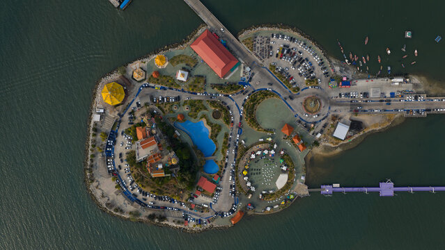 Aerial view of Koh Loi island featuring its temple complex, parking areas, small park, and pedestrian bridge connecting to the mainland in Si Racha, Chon Buri, Thailand.