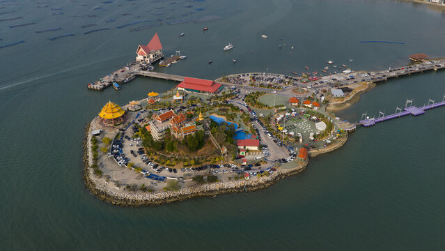 Aerial view of Koh Loi temple complex surrounded by the sea with a long pier, parking areas, and lush greenery in Si Racha, Chon Buri, Thailand.