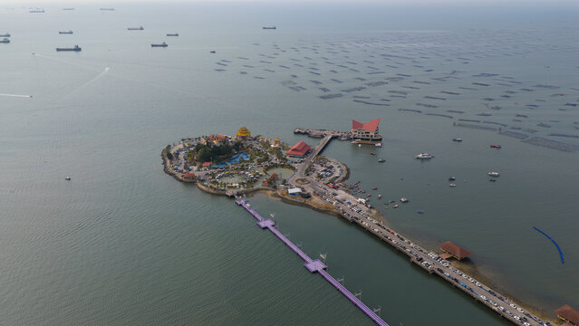 Aerial view of Koh Loi island featuring its temple, bridge, and parking area surrounded by the sea with boats and aquaculture nets in Si Racha, Chon Buri, Thailand.