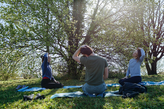 Three Friends Practicing Seated Neck Stretch During Outdoor Yoga Session in Park