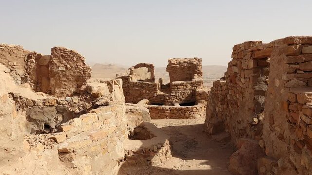 Sun-drencher ancient ruins of traditional fortified structures of Ksar Beni Barka with remains of mud brick rooms used for dwelling and granaries, Tataouine, Tunisia