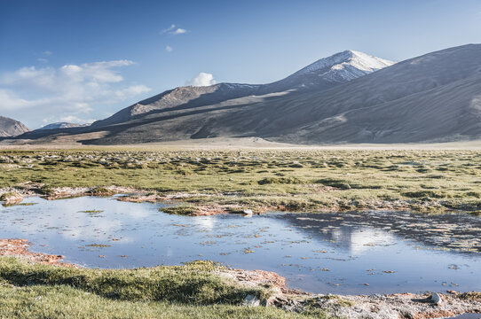 Clear-water rivers and lakes in a mountain valley, pastures and green grassy fields set against mountain ranges and snow-capped, glacier-clad peaks&mdash;a scenic landscape background