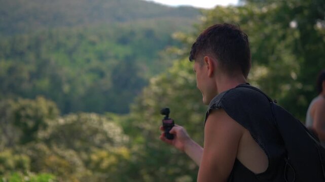 Male traveler filming tropical rainforest mountains with pocket camera during jungle adventure, Travel creator capturing lush forest scenery, mountain wilderness and tropical nature 4k