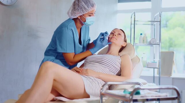 Woman doctor in disposable mask gives injection and performs procedure of lip augmentation of girl patient in cosmetology clinic. Correction of asymmetry, lip volume increase