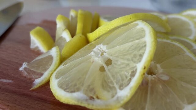 Close up view of fresh organic lemon slices piled on a round wooden cutting board in a kitchen, representing healthy eating, vitamin c, refreshing ingredients, and preparing food