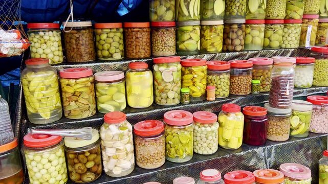 Assorted pickled fruits displayed in glass jars and trays. These tangy snacks are perfect for relaxing or leisure time. Sold at night markets, custo