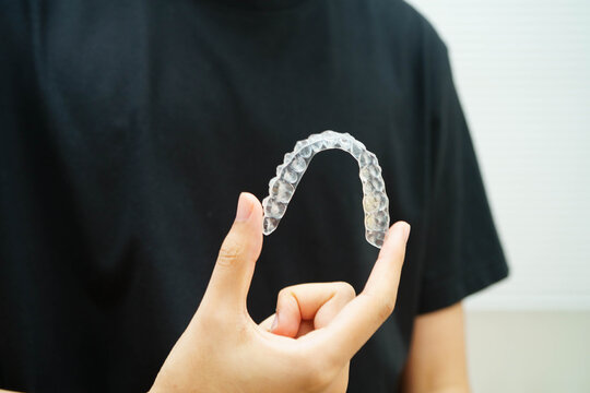 Man holding invisible aligner orthodontic retainer for dental teeth straightening.