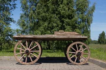 Obraz premium Vintage Wooden Wagon Cart On Pavement With Rustic Spoked Wheels Against Lush Countryside