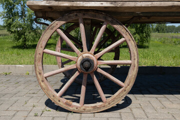 Obraz premium Rustic Wooden Wagon Wheel On Old Cart In Countryside Summer Landscape