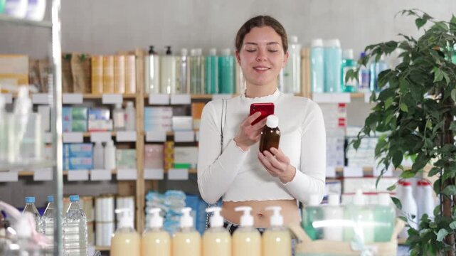 Young woman scans a barcode on a bottle of medicinal syrup in front of a medicine counter in the pharmacy with a mobile phone . High quality 4k footage