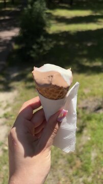 Close up of a female hand with a beautiful manicure holding a chocolate and vanilla ice cream cone that is melting in the summer sun, enjoying a refreshing sweet snack outdoors in a park