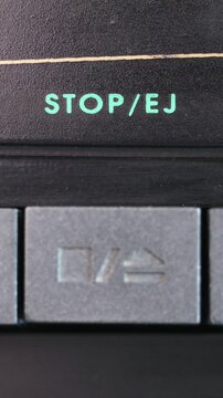 Vertical close up of gray stop eject button being pressed below turquoise STOP EJ text
