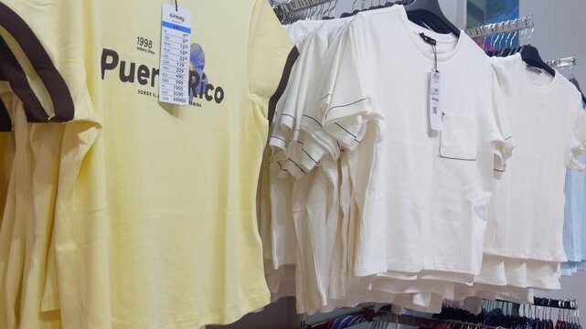 Clothing store display featuring a collection of summer t shirts with price tags hanging on a rack, showcasing various colors and styles available for purchase