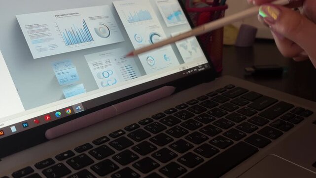 Businesswoman analyzing company financial report data on laptop screen while pointing at diagrams and charts with a pencil, working on a presentation in a modern office