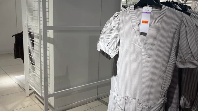 Retail clothing store display featuring striped shirts and dresses on hangers in a modern shopping mall aisle with a price tag visible on new merchandise