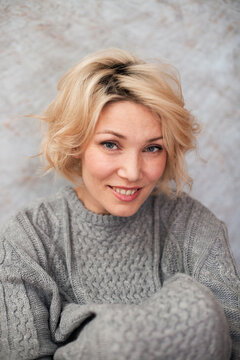 Blonde woman in a gray knitten sweater indoor portrait.