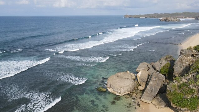 Aerial view of Indrayanti Beach with rocky cliffs, turquoise water, and breaking waves in Kecamatan Tepus, Daerah Istimewa Yogya, Indonesia.