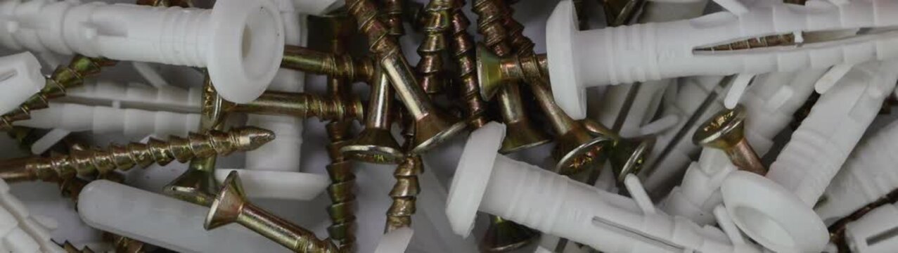 Assortment of metal screws and white plastic wall plugs for home improvement projects and renovation work.