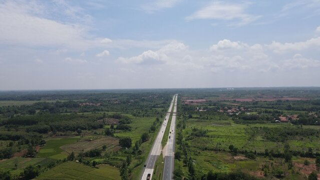 Aerial view of the toll road stretching through the lush green rural landscape and agricultural fields of Cipeundeuy, West Java, Indonesia.