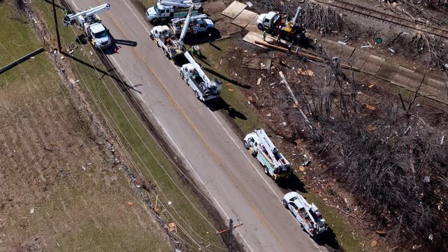 Aerial drone view of utility crews repairing damaged power lines after a severe storm or tornado. Bucket trucks and electrical workers restoring the power line