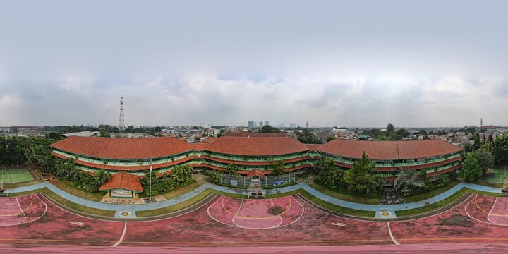Aerial view of the school building at Pondok Labu featuring red tiled roofs, green walls, and a surrounding sports court under a cloudy sky in Cilandak, Jakarta, Indonesia.