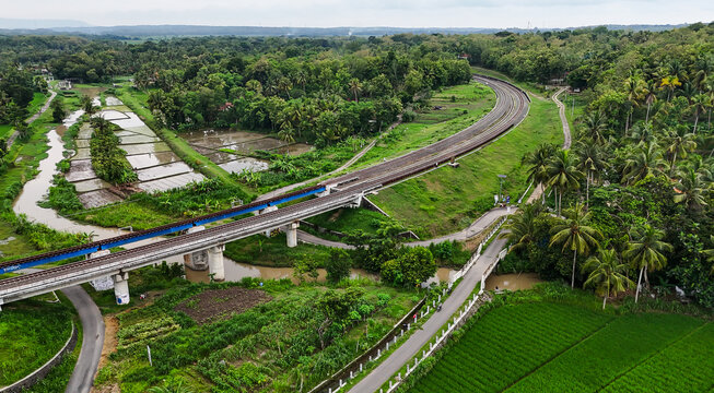 Aerial view of a straight railway track cutting through a lush green tropical forest.