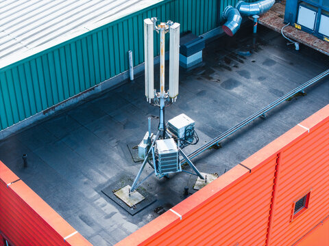 Aerial view of a cellular base station antenna mounted on a flat rooftop with orange and green metal walls in Riga, Latvia.