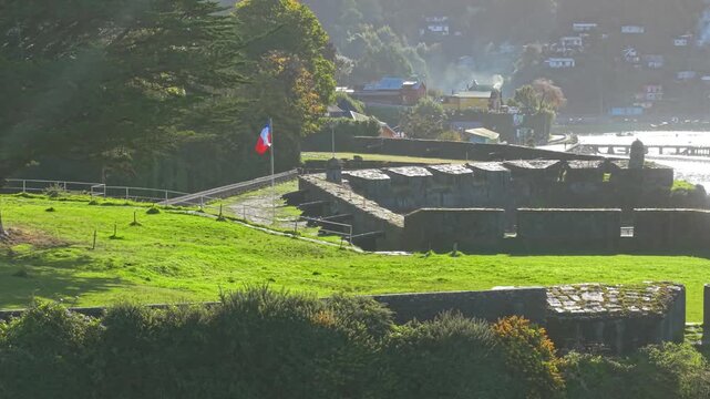 Telephoto aerial orbit of a row of cannons at San Sebastian de la Cruz Castle in Corral, Valdivia, Chile a stone defensive fortification with a Chilean flag.