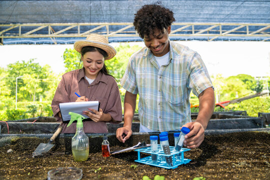 Smiling agricultural students collect soil samples with test tubes and note for soil analysis in agricultural laboratory for farm science project. Smart agriculture experiment by young team.