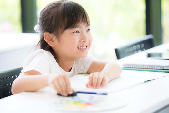 A young girl, around kindergarten or elementary school age, concentrating on her studies while looking at the blackboard in a classroom&mdash;at a cram school or school, preparing for entrance exams, studyi
