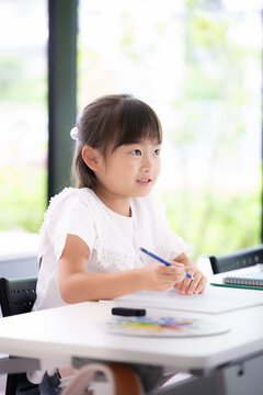 新緑の教室で黒板を見る勉強に集中して取り組む幼稚園・小学生位の女の子・塾や学校、受験や勉強、学習の勉強がわかった！ポジティブイメージ　縦