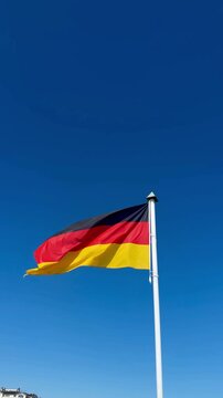 The German flag flutters in the wind against a blue sky.