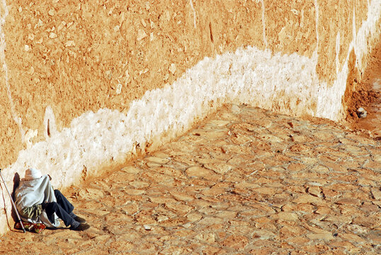 Algeria, Ben Isguen, man wrapped in blanket sitting in front of a wall