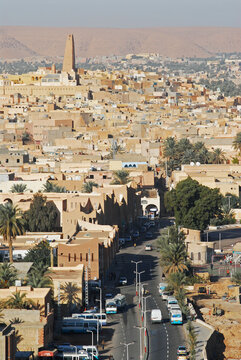 Algeria, Ghardaia, view of city with vehicles on road, mud-brick dwelling and tall minaret against clear sky
