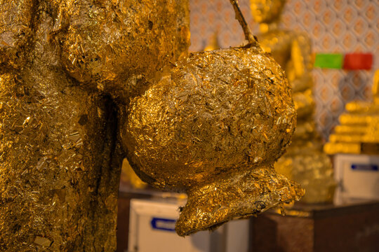 Gold leaf gilded statue closeup golden texture religious shrine temple interior worship Buddhism sacred offering on sculpture surface warm light spiritual devotion